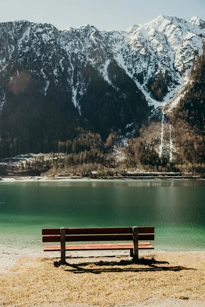 A photo of a bench by a lake with mountains in the distance. alt_text